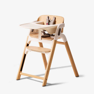 Silla de comer evolutiva 5 en 1 DinerPal Momcozy en madera de haya con bandeja blanca y arnés de 5 puntas, vista en ángulo sobre fondo claro
