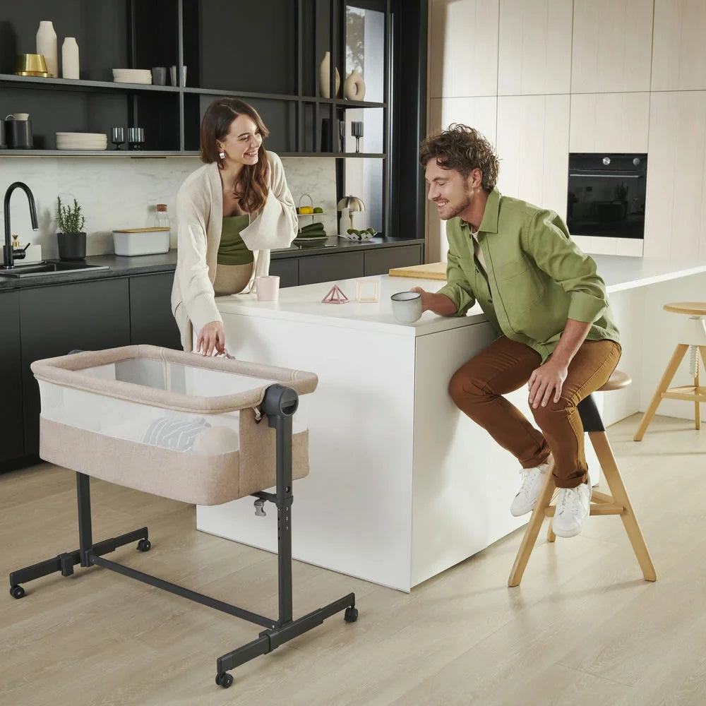 Padres en la cocina junto a la cuna colecho Nestee Up 2 Kinderkraft sobre sus ruedas