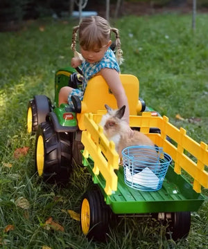 niña pequeña montada en tractor eléctrico miniatura de john deere con un conejo en la parte de atrás y una canasta para recoger huevos
