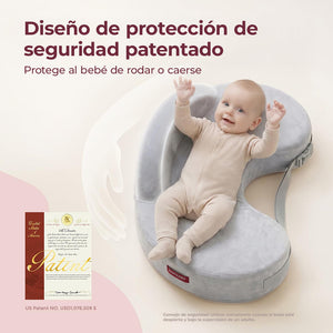 Bebé sonriendo con los brazos arriba, recostado en un cojín de lactancia Momcozy gris con diseño de protección que evita que ruede o se caiga, junto al certificado de patente