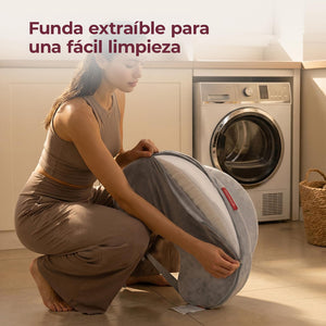 Mamá sentada en un sillón alimentando a su bebé con mamadera sobre un cojín de lactancia Momcozy gris con superficie un 28% más amplia, comparado con una mamá que sostiene a su bebé con un cojín tradicional