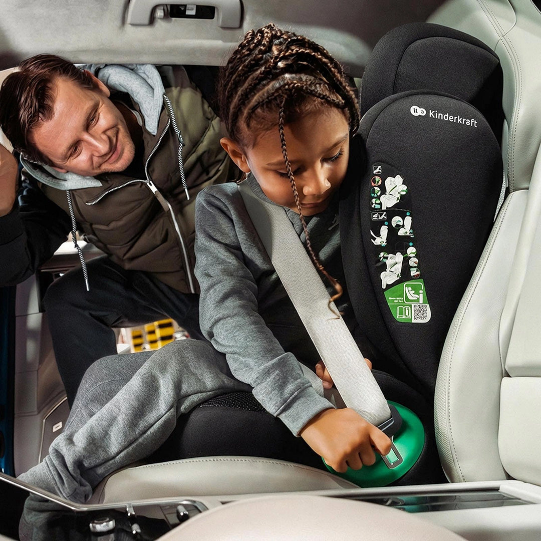 Silla de auto Butaca Junior Fix 2 Plus i-Size Kinderkraft color gris, niña con trenzas abrochando el cinturón de seguridad con ayuda de un adulto, se aprecia la etiqueta de instalación con código QR