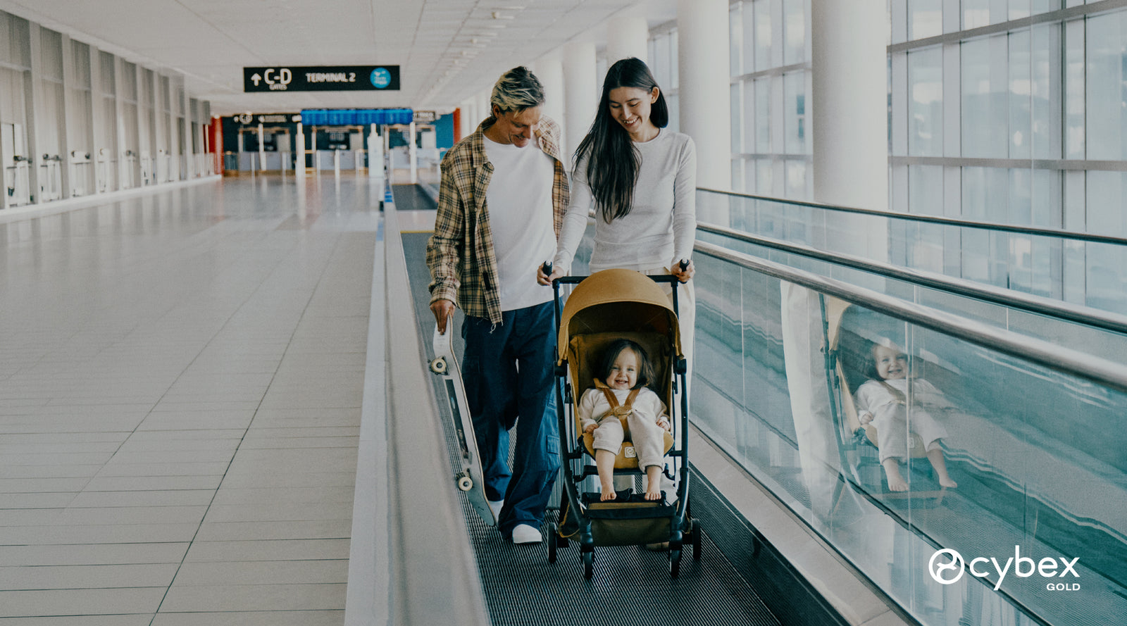 mujer y hombre en la banda metálica del aeropuerto junto a niña pequeña en coche de paseo Libelle ultracompacto Cinnamon Yellow de Cybex Gold