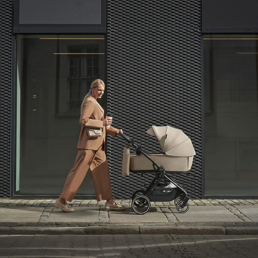 Coche cuna Yoxi 2 en 1 Kinderkraft color beige, mujer paseando por la ciudad con el coche en modo moisés