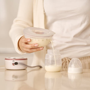 Mano de mujer vertiendo leche desde extractor hacia mamadera, usando Extractor de Leche V1 Pro Doble Series de MOMCOZY 