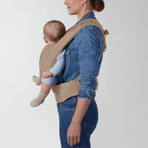 Portabebé Coÿa color Cozy Beige - vista lateral con bebé en posición de porteo en la espalda