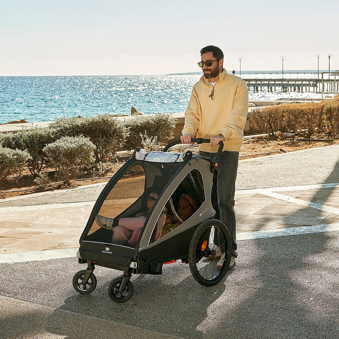 Padre empujando el Nava Walk 2 en 1 Kinderkraft en modo coche de paseo con dos niñas sentadas en su interior