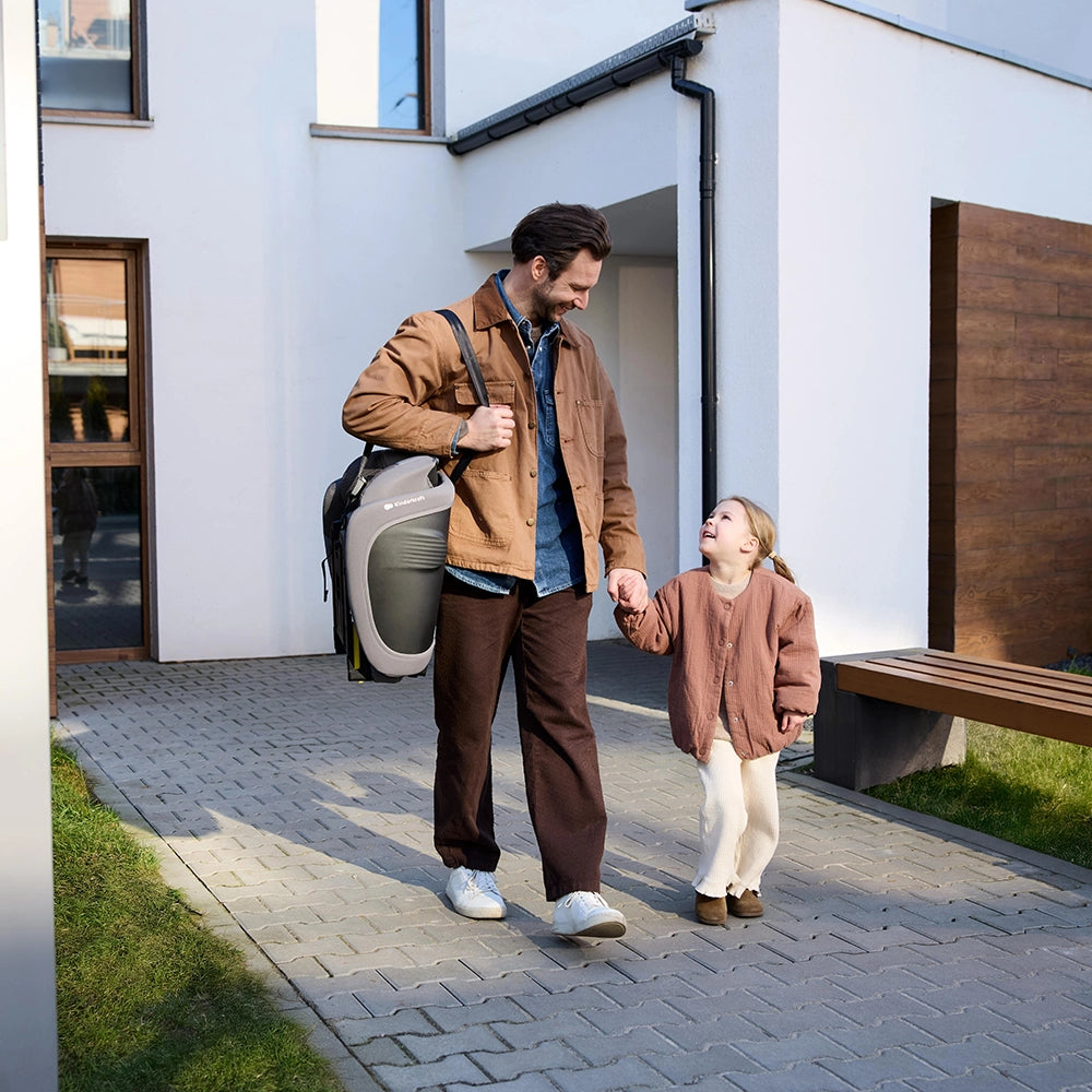 Hombre cargando la silla de auto Combinada Fix2Go i-Size Kinderkraft color gris topo sobre el hombro mientras camina de la mano con su hija
