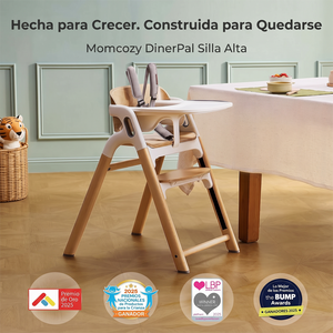 Silla de comer DinerPal Momcozy con bandeja y arnés junto a una mesa de comedor, con los sellos de premios 2025 Premio de Oro, Premios Nacionales de Productos para la Crianza, Loved by Parents y The Bump Awards