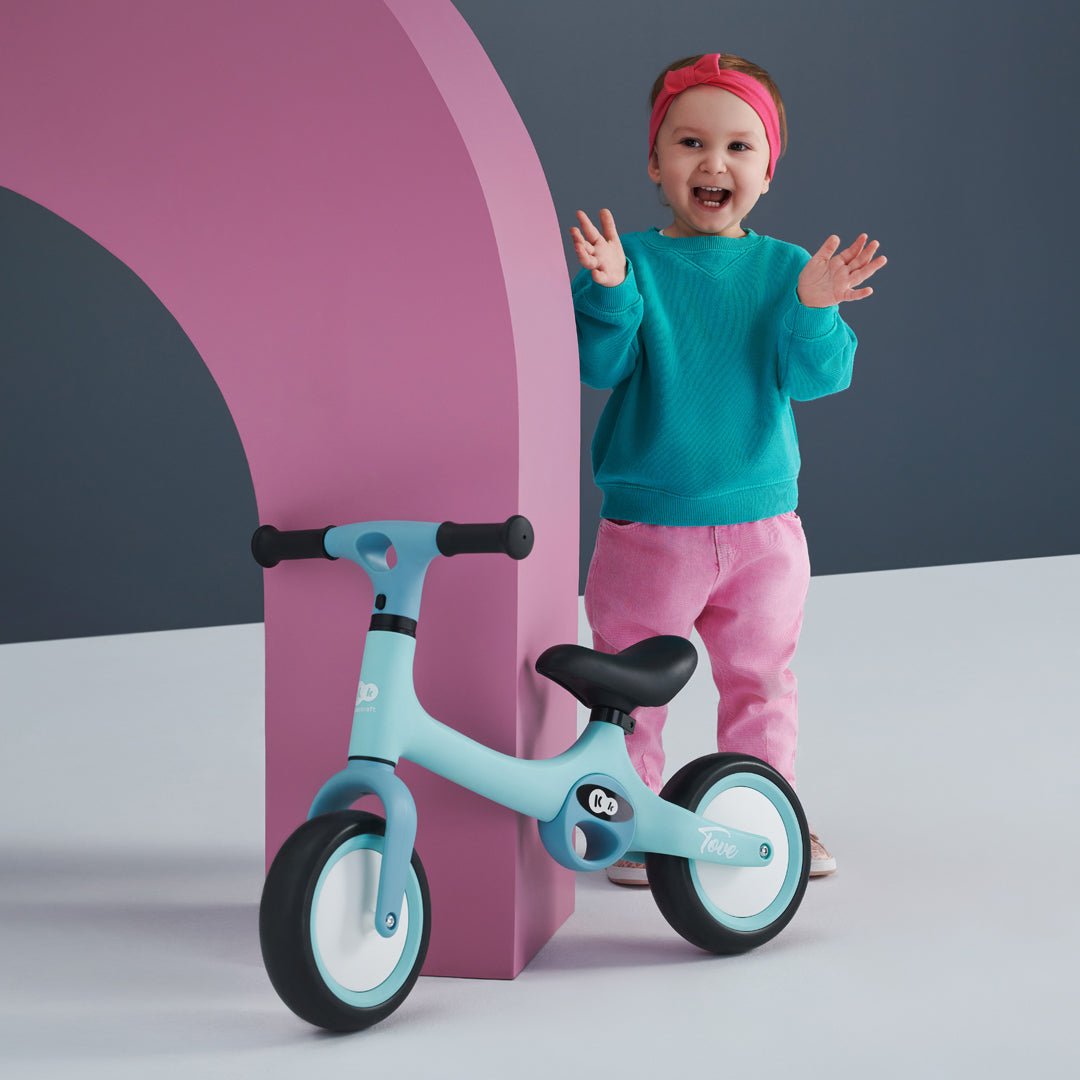 Niña pequeña contenta junto a Bicicleta de balance Tove color celeste de Kinderkraft